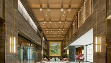 A spacious lobby with a high ceiling, marble walls, and a large painting.