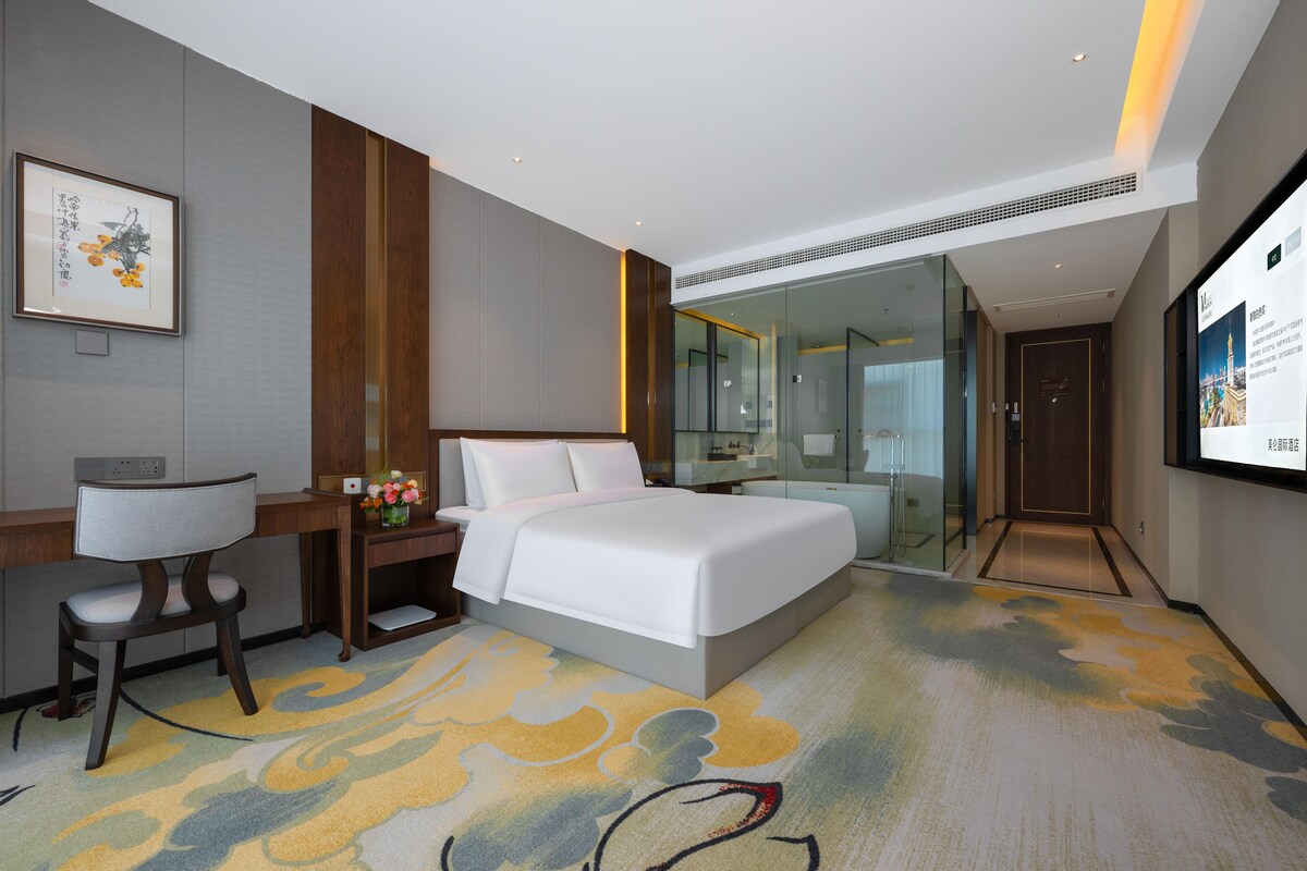 A hotel room with a bed, desk, chair, and a large mirror.