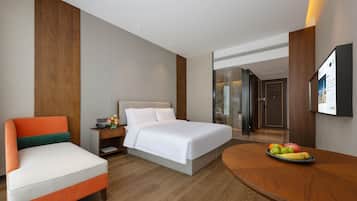 A hotel room with a bed, a chair, a desk, and a fruit bowl.