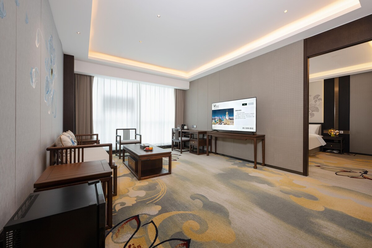 A hotel room with a large bed, a desk, a television, and a seating area with a view of the city.