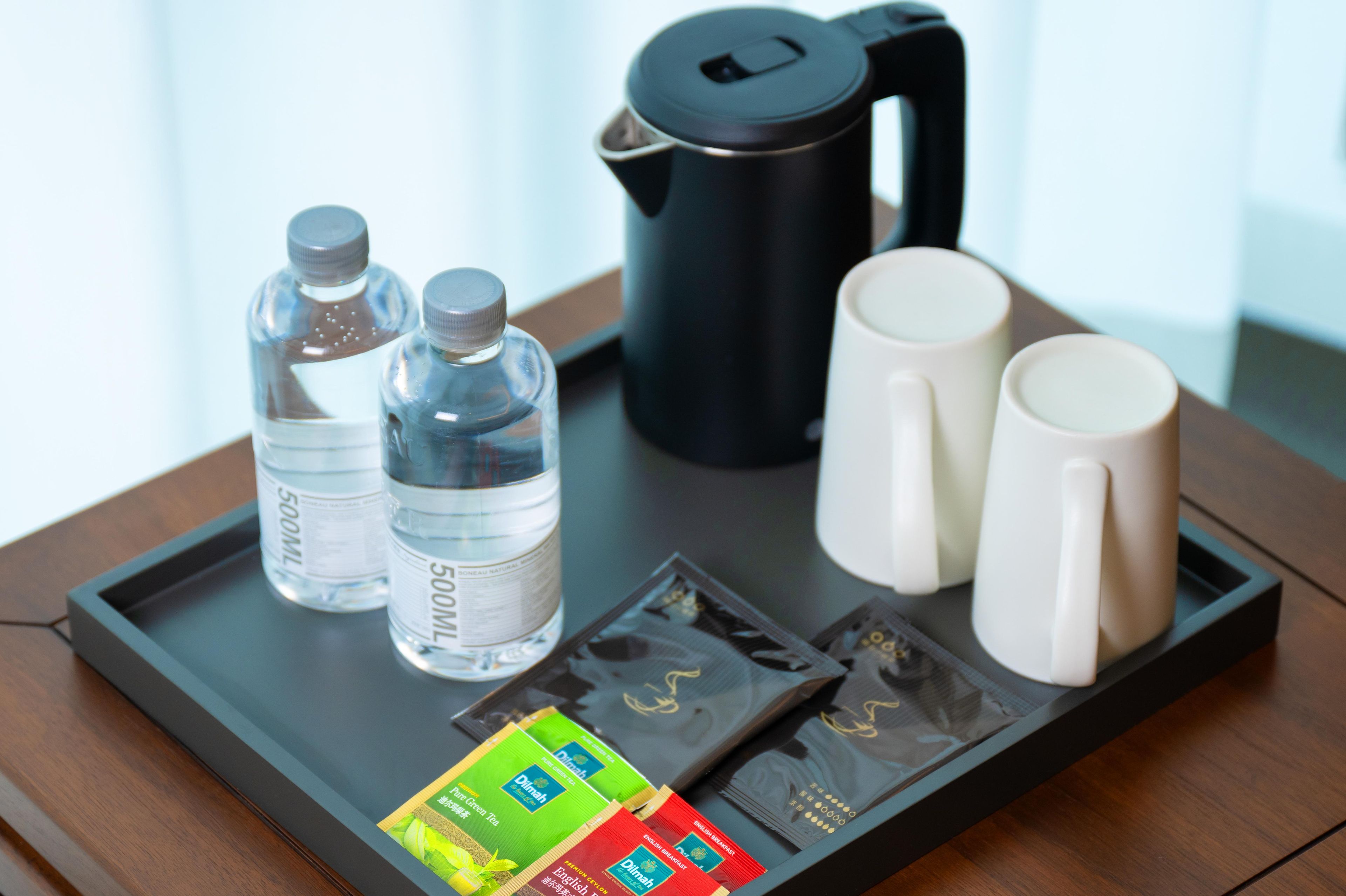 A tray with two water bottles, a coffee maker, two mugs, and packets of snacks.