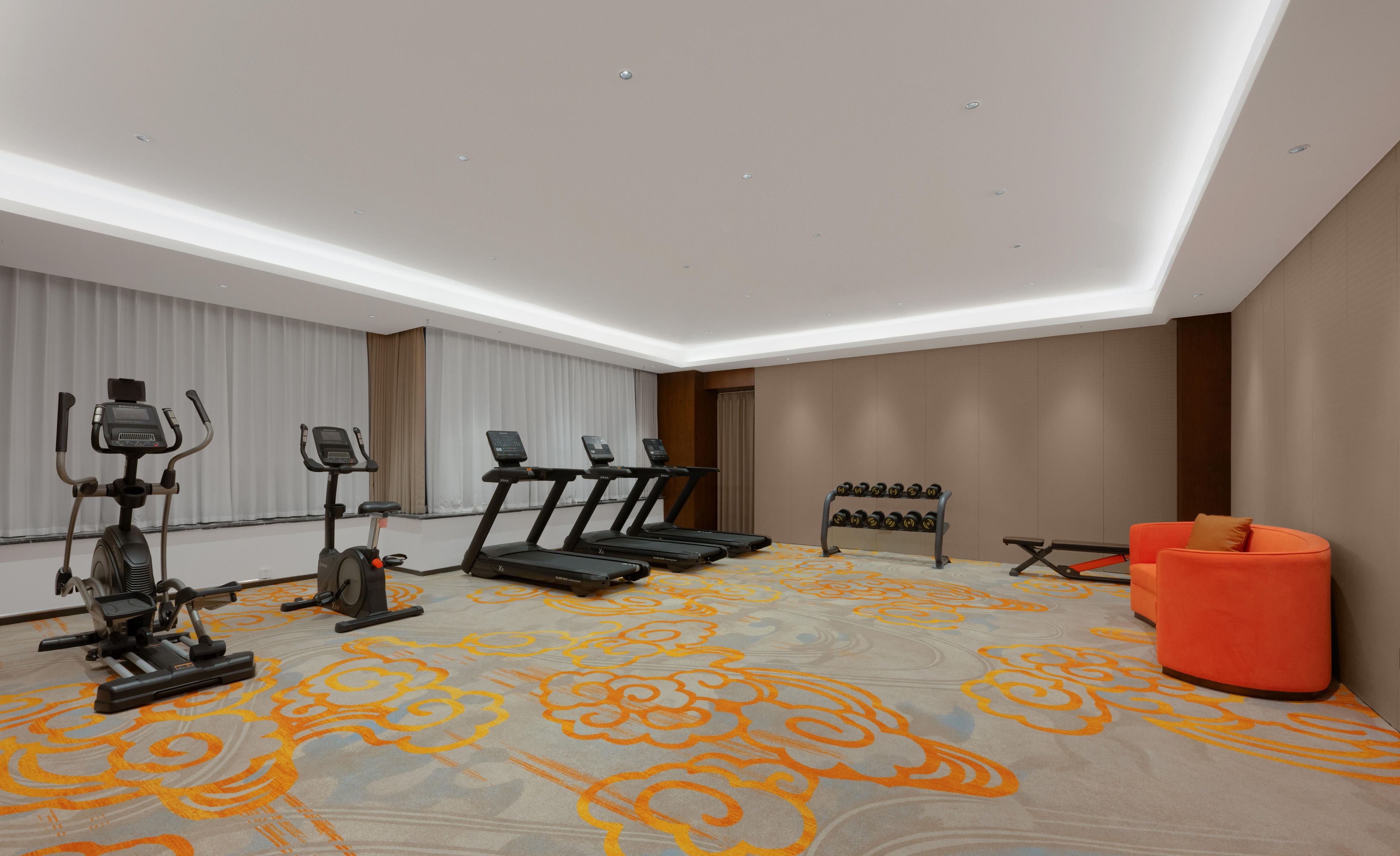 Une chambre d’hôtel moderne dotée d’un espace de remise en forme comprenant des tapis de course, un appareil elliptique et un ensemble d’haltères.