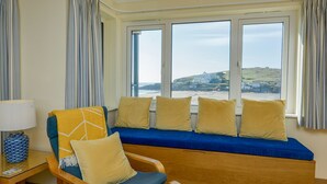 A room with a wooden bench and a chair, a table with a lamp, and a view of the sea through large windows. - 12 Burgh Island Causeway (Kingsbridge)