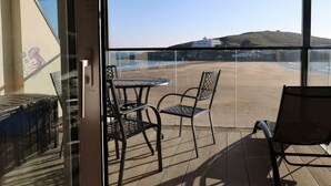 A balcony with two metal chairs and a small table, overlooking a parking area and distant buildings. - 12 Burgh Island Causeway (Kingsbridge)