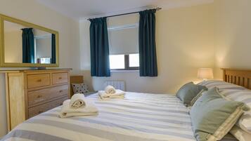 Een slaapkamer met een bed, een kaptafel, een spiegel, een raam met gordijnen en een bedlamp.
