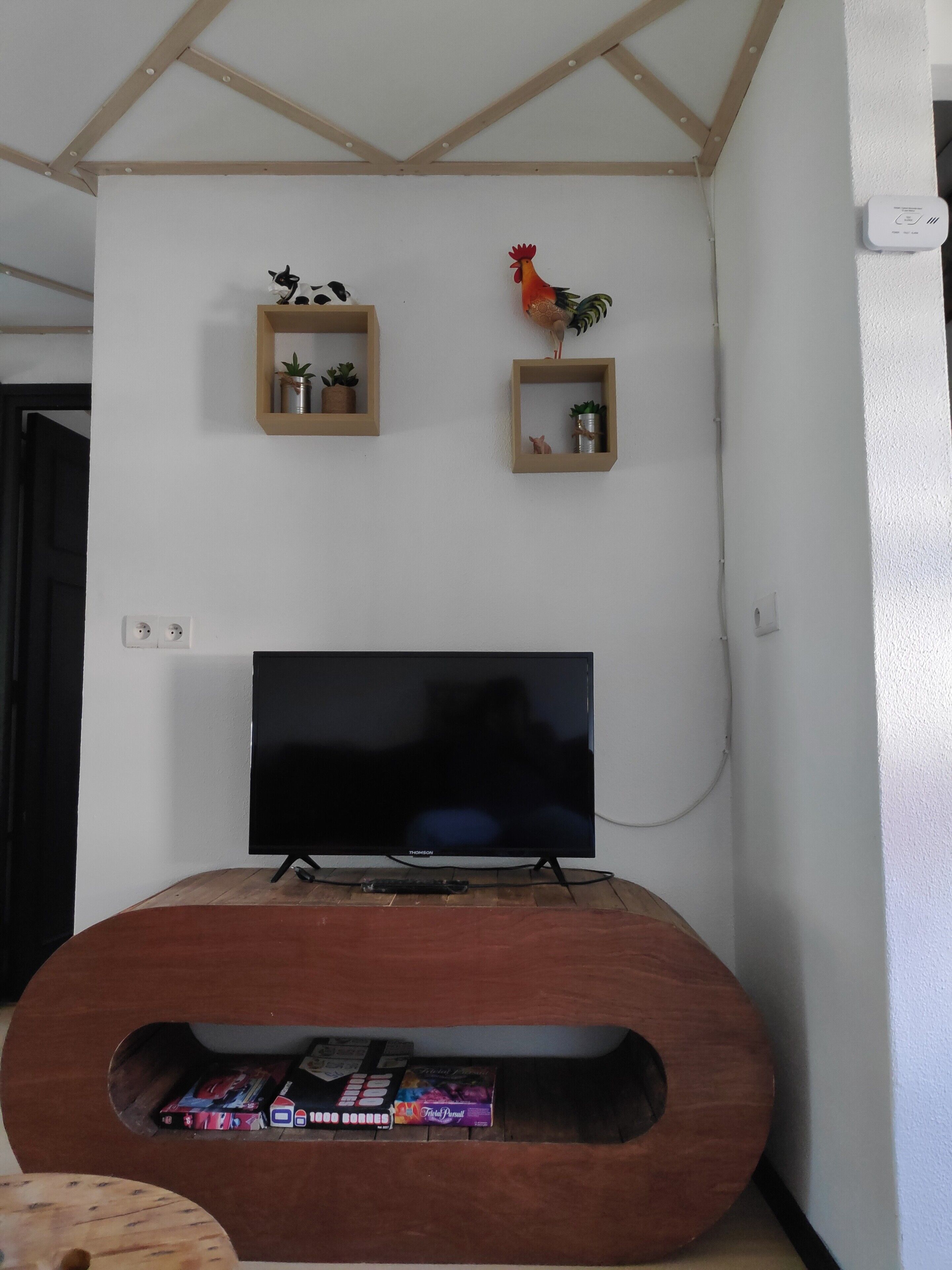 A living room with a flat-screen TV, wooden shelves with decorative items, and a built-in entertainment unit with a magazine rack.