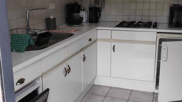 A kitchen with white cabinets, a stove, a sink, and a clock on the wall.