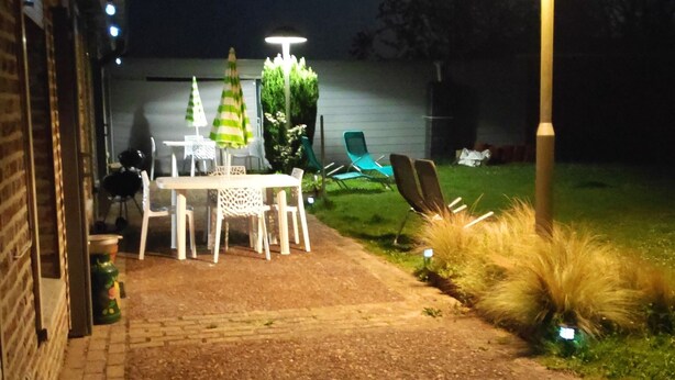 Een terras buiten met een tafel en stoelen, een pad en een hoge straatlamp.
