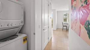 A laundry room with a front-loading washer and dryer, a door leading to a dining area, and a painting on the wall. - Lido Dream Combined Duplex Both N & S (Sarasota)