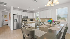 A modern kitchen with white cabinets, stainless steel appliances, and a dining area with a wooden table and chairs. - Lido Dream Combined Duplex Both N & S (Sarasota)