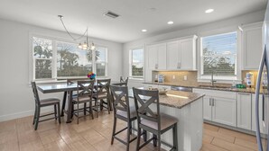 A modern kitchen with white cabinets, a granite countertop, and a dining area with dark wooden chairs. - Lido Dream Combined Duplex Both N & S (Sarasota)