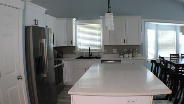 A modern kitchen with white cabinets, a stainless steel refrigerator, and a large island. - Spacious 5-bedroom house in charming Stansbury Park with WiFi, AC (Stansbury Park)