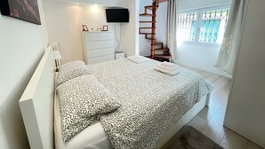A bedroom with a bed, a white dresser, a TV mounted on the wall, a wooden spiral staircase, and a window with curtains. - Tranquility and comfort near Careggi, 10 min from center by tramway (Firenze)