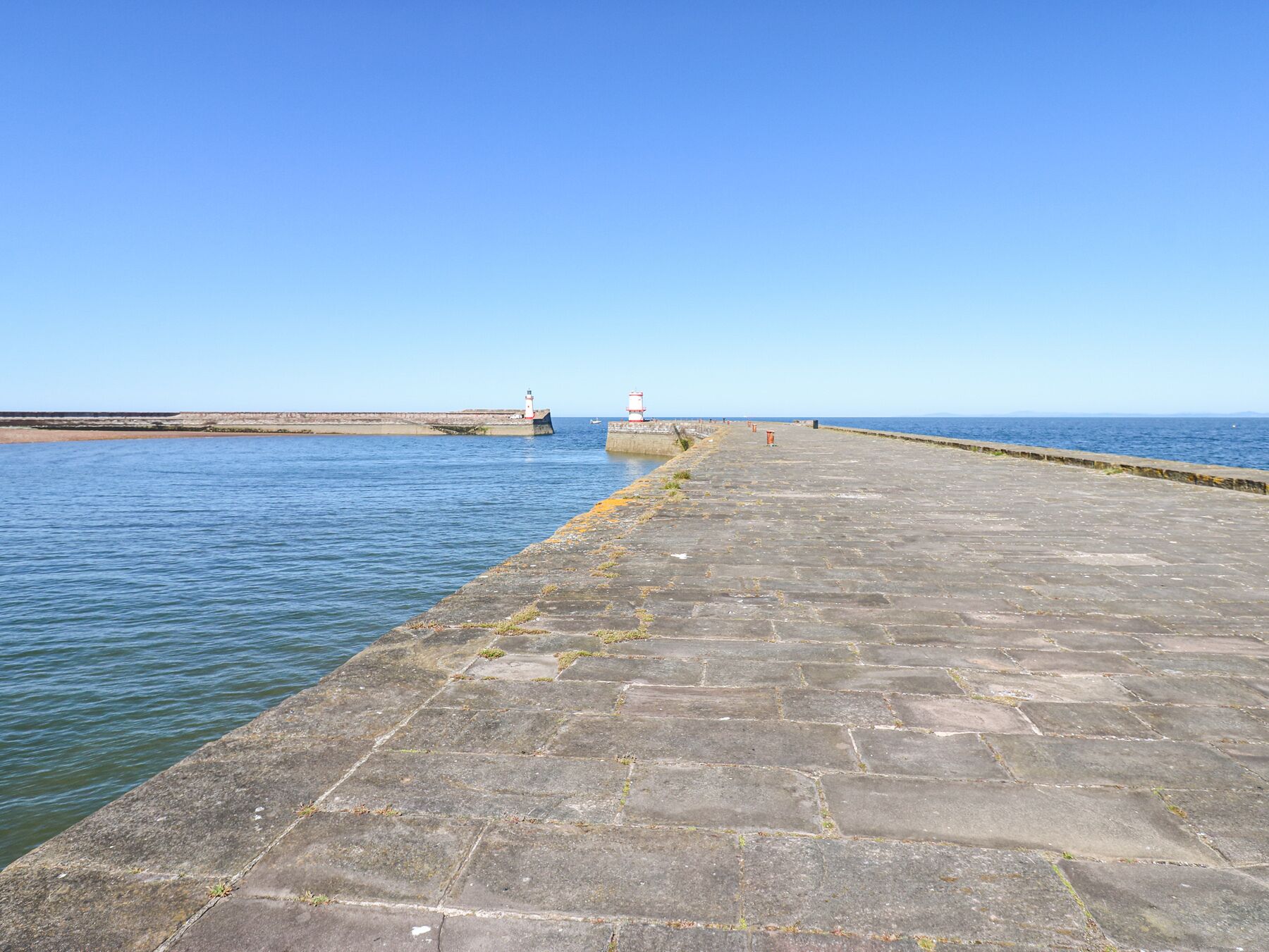 Een lange, rechte stenen pier die zich uitstrekt over kalm water, met een heldere lucht erboven.