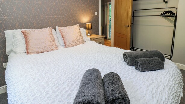 A neatly made bed with pillows, a bedside lamp, and a towel rack with towels. - Flat 2, Omega Court (Whitehaven)