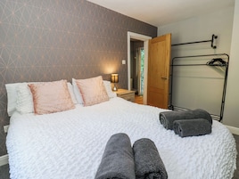 Een net opgemaakt bed met kussens, een bedlampje en een handdoekrek met handdoeken.
