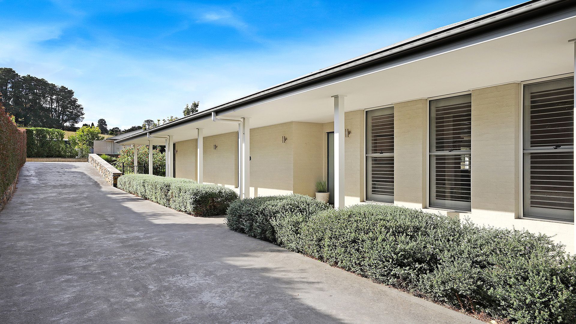A row of modern, single-story buildings with a covered walkway and neatly trimmed hedges.