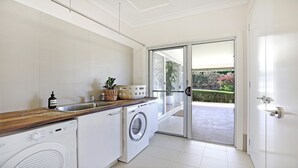 A modern kitchen with a washing machine, a sink, and a window leading to a balcony. - Albert Fields - stylish family-friendly retreat in the Southern Highlands (Bowral)