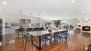 Un amplio salón con mesa de comedor de madera, sillas negras, chimenea y un ventanal con vistas al exterior.