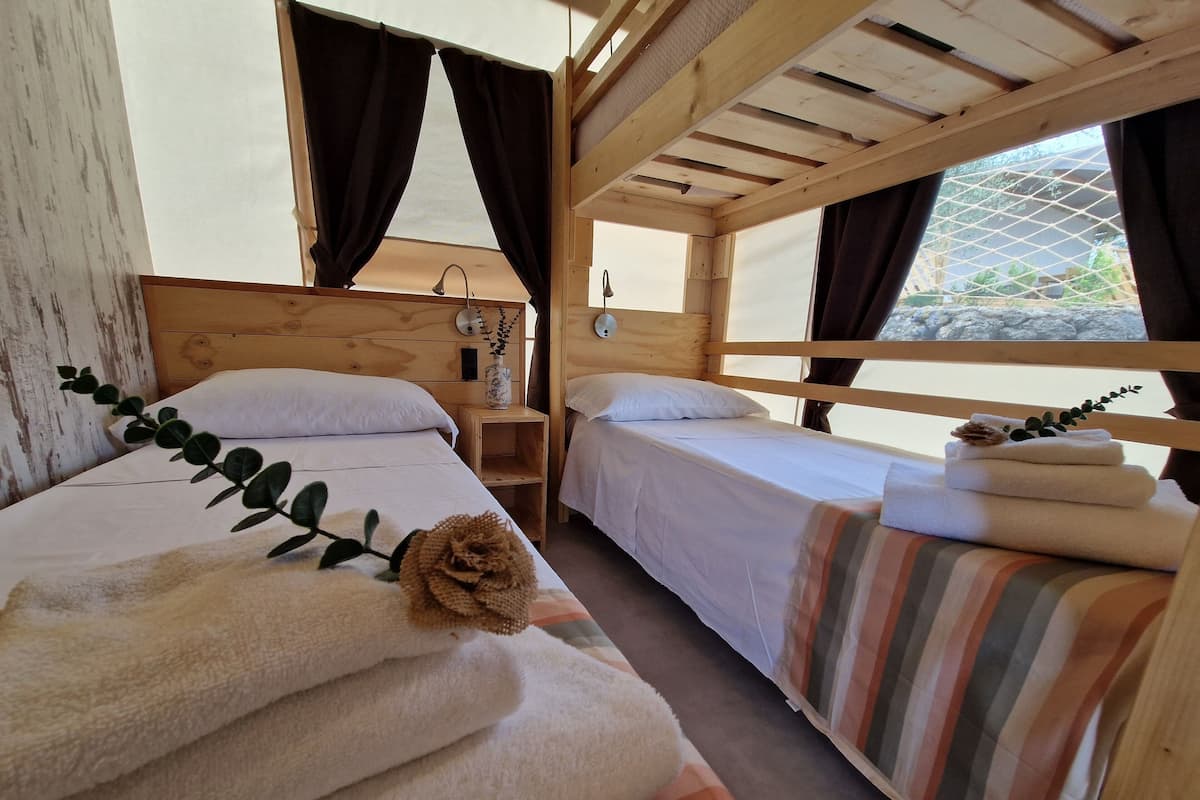 Une cabine équipée de deux lits superposés en bois, chacun avec une literie blanche et une petite table de chevet.