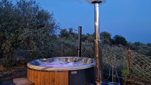 A hot tub with a chimney emitting smoke, surrounded by gravel and wooden steps, set against a backdrop of trees and a clear sky. - Koru (Belpasso)