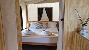A neatly made bed with white linens and striped pillows, a bedside table with a lamp, and a vase with a plant on the right side. - Koru (Belpasso)