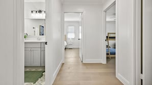 Un couloir étroit, avec un coin cuisine sur la gauche, une chambre avec un lit superposé sur la droite, et une porte donnant sur une autre pièce.