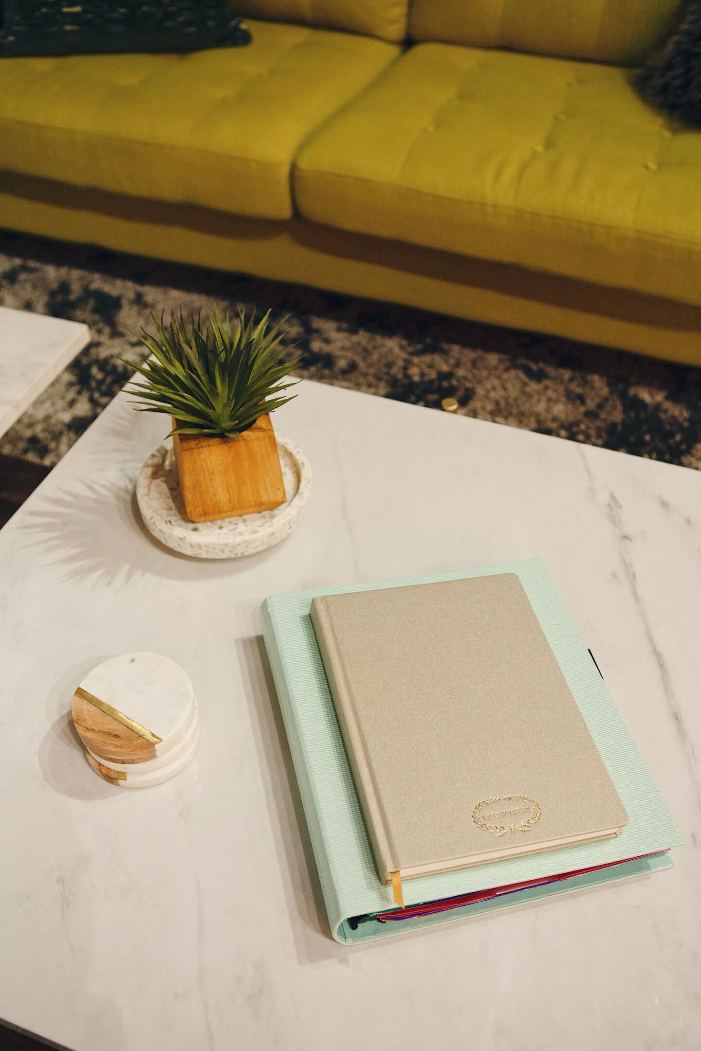 Una mesa de centro de mármol blanco con una pequeña planta en maceta, un adorno y un cuaderno cerrado.