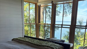 A bedroom with a large bed, wooden floor, and a view of a lake through large windows.