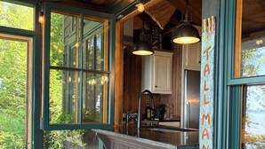 A rustic cabin interior with a wooden ceiling, large windows, a bar area, and a seating bench.