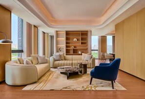 Un salon moderne avec un canapé incurvé, un fauteuil bleu et une table basse. On y trouve une bibliothèque agrémentée d’objets décoratifs, et de grandes fenêtres offrent une vue sur la ville.