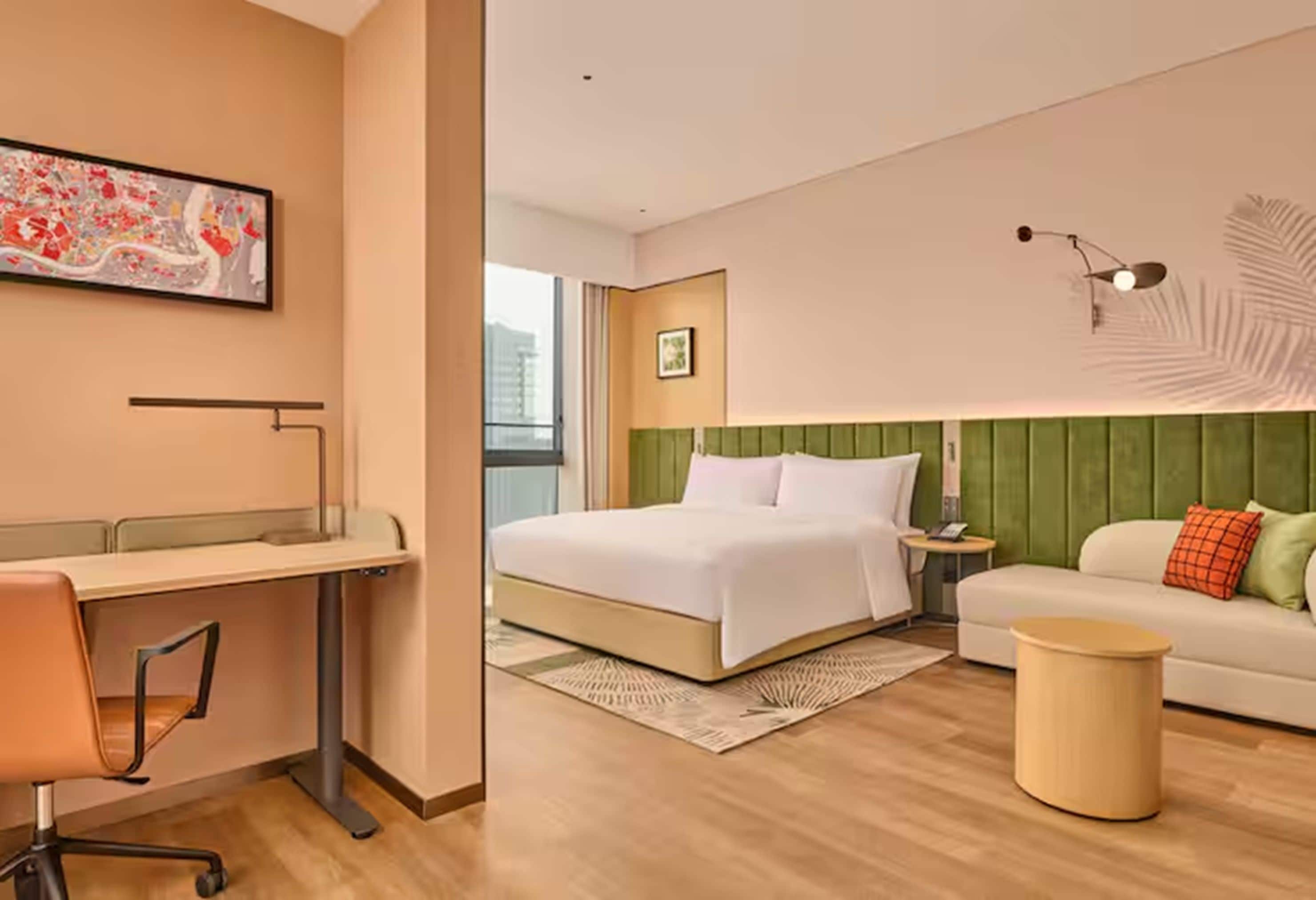 Ein Hotelzimmer mit einem Bett, einem Schreibtisch, einem Stuhl und einem grünen Polstersofa.
