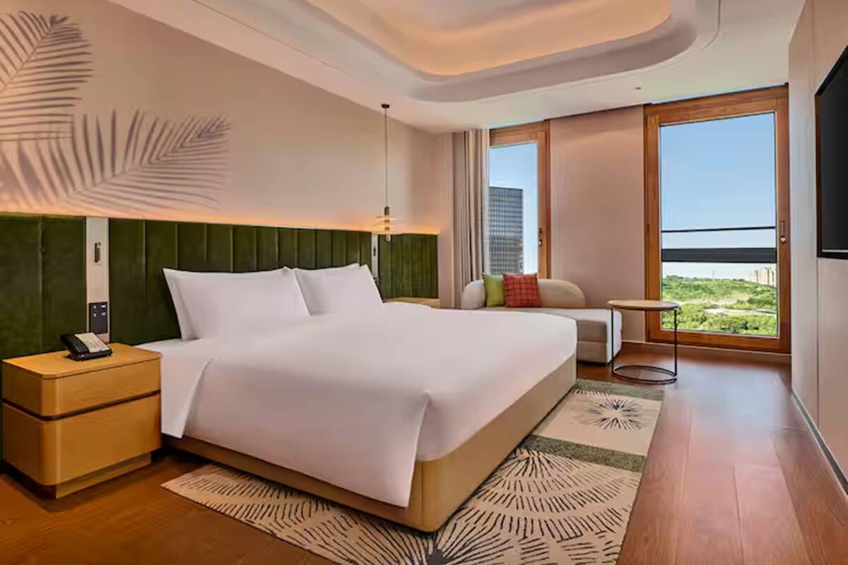 Ein Hotelzimmer mit einem großen Bett, einem Nachttisch, einem kleinen Tisch, einer Couch und einem großen Fenster mit Blick auf die Stadt.