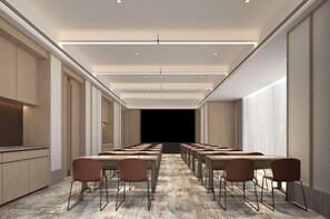 A conference room with long tables and chairs, a stage at the front, and a kitchen area to the left. - Hilton Garden Inn Chongqing Yubei Central Park (Chongqing)
