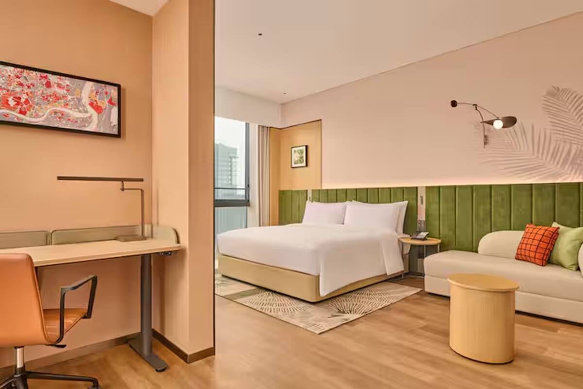 Ein Hotelzimmer mit einem Bett, einem Schreibtisch, einem Stuhl und einem grünen Polstersofa.