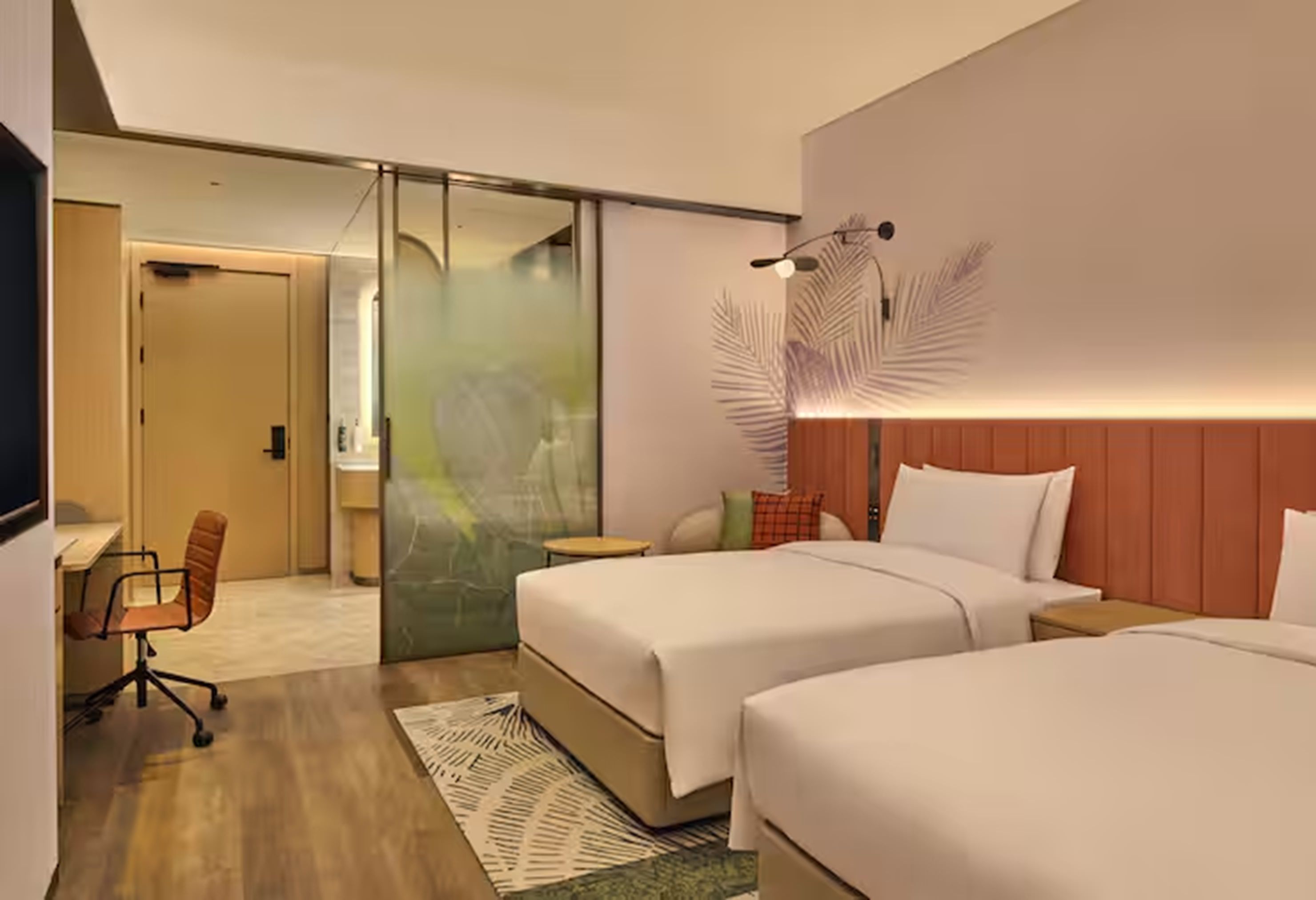 Une chambre d’hôtel avec deux lits, un bureau, une chaise et une porte coulissante donnant sur une autre pièce.