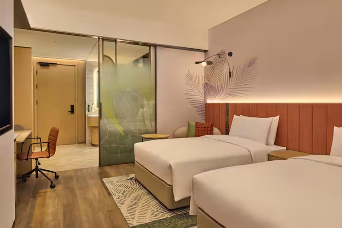 A hotel room with two beds, a desk, a chair, and a sliding door leading to another room.