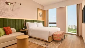 A modern hotel room with a large bed, a sofa, a round side table, and a view of a cityscape through a large window. - Hilton Garden Inn Chongqing Yubei Central Park (Chongqing)