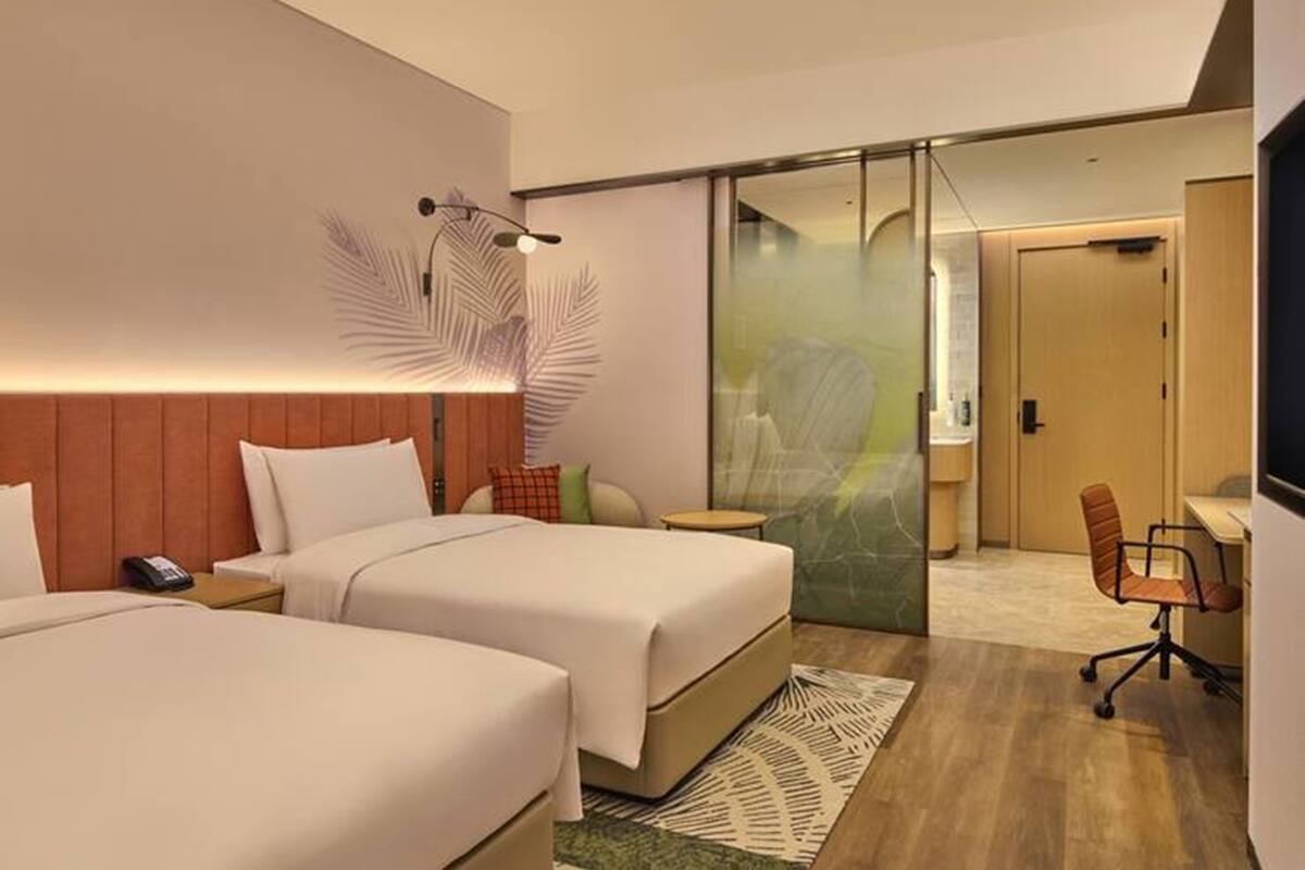 Ein Hotelzimmer mit zwei Betten, einem Schreibtisch, einem Stuhl und einem großen Spiegel.