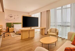 A modern hotel room with a flat-screen TV, a sofa, a round coffee table, and a large window with sheer curtains. - Hilton Garden Inn Chongqing Yubei Central Park (Chongqing)