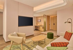 A modern hotel room with a sofa, armchair, and a small round table. There is a desk with a chair and a television mounted on the wall. - Hilton Garden Inn Chongqing Yubei Central Park (Chongqing)
