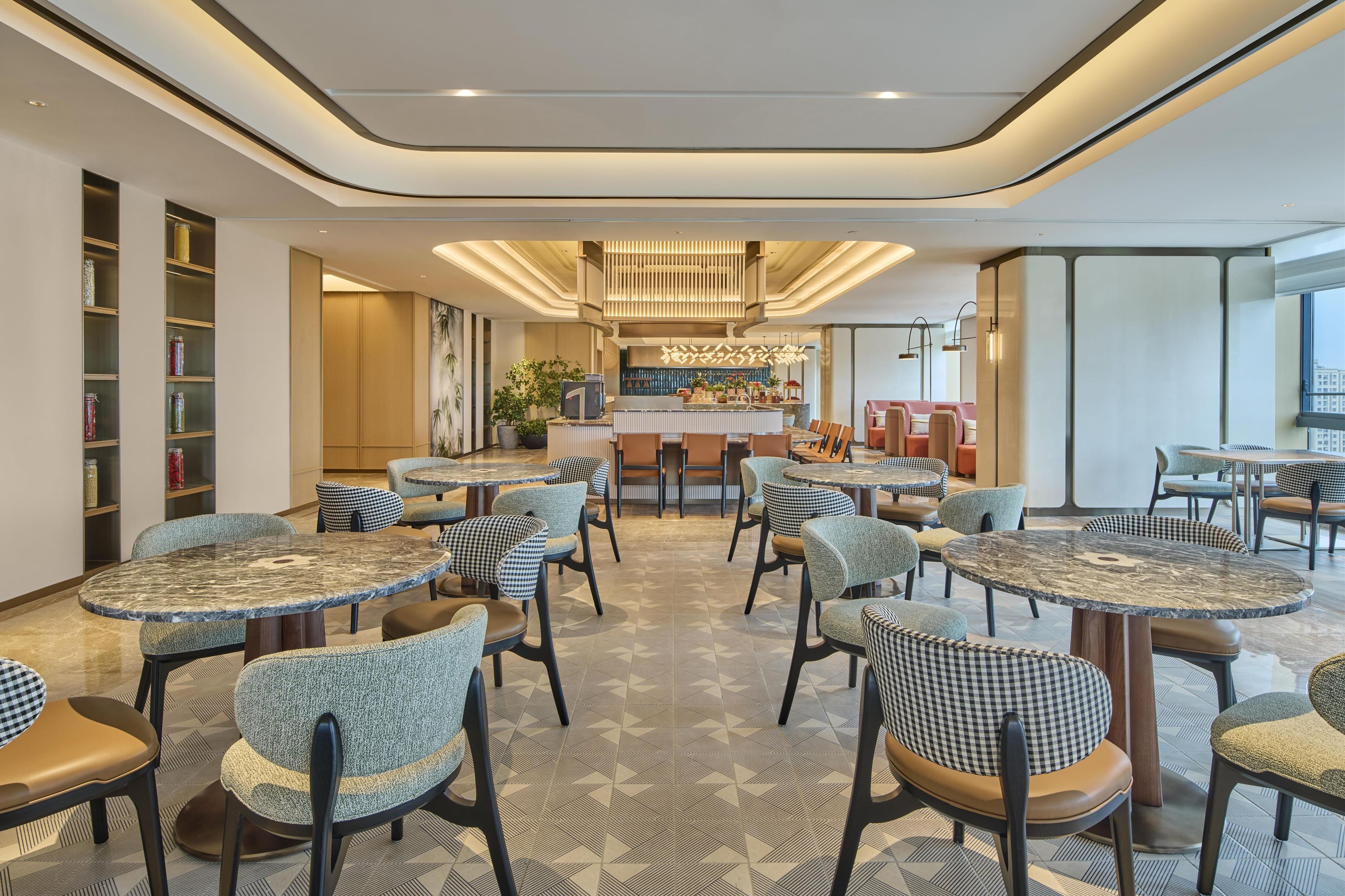 A modern hotel lobby with round tables and chairs, a bar area, and a large window offering a view.