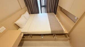 A compact bed with a pull-out drawer, a bedside table, and a window with curtains.