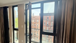 A room with large windows, a door, and a view of red brick buildings outside.