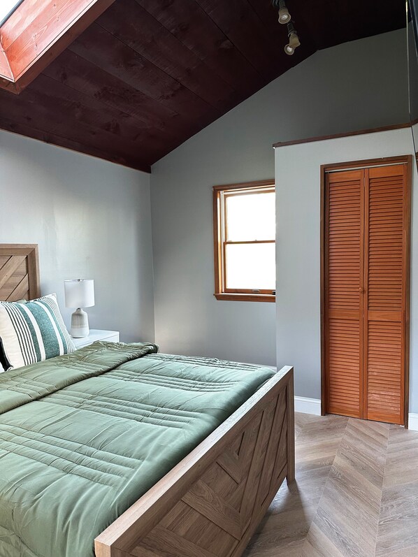 Un dormitorio con cama, mesita de noche, lámpara, ventana y armario de madera.