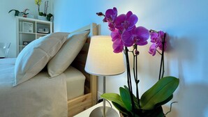 A bedroom with a bed, pillows, a bedside table with a lamp, and a potted orchid plant. - Martinengo30 Apartment Milano - Balcony,Wifi and near Metro M3 (Milano)