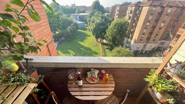 A balcony with a view of a green park and buildings, a wooden table with chairs, and various potted plants. - Martinengo30 Apartment Milano - Balcony,Wifi and near Metro M3 (Milano)
