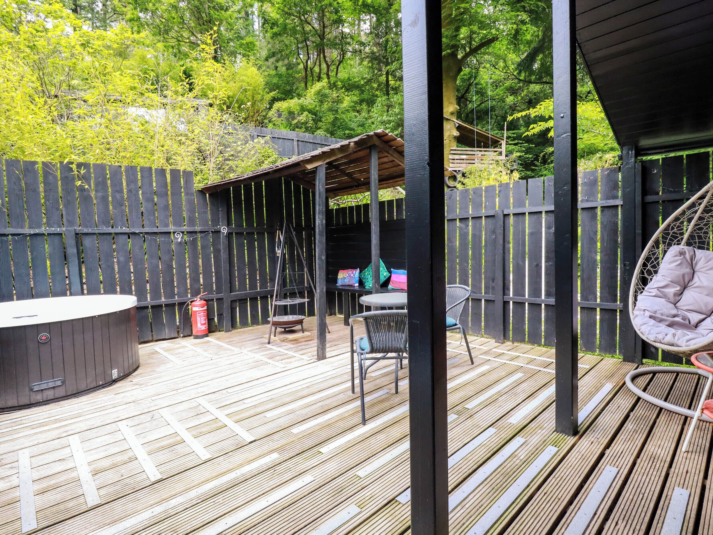 A wooden deck with a hot tub, outdoor seating, and a swing chair.