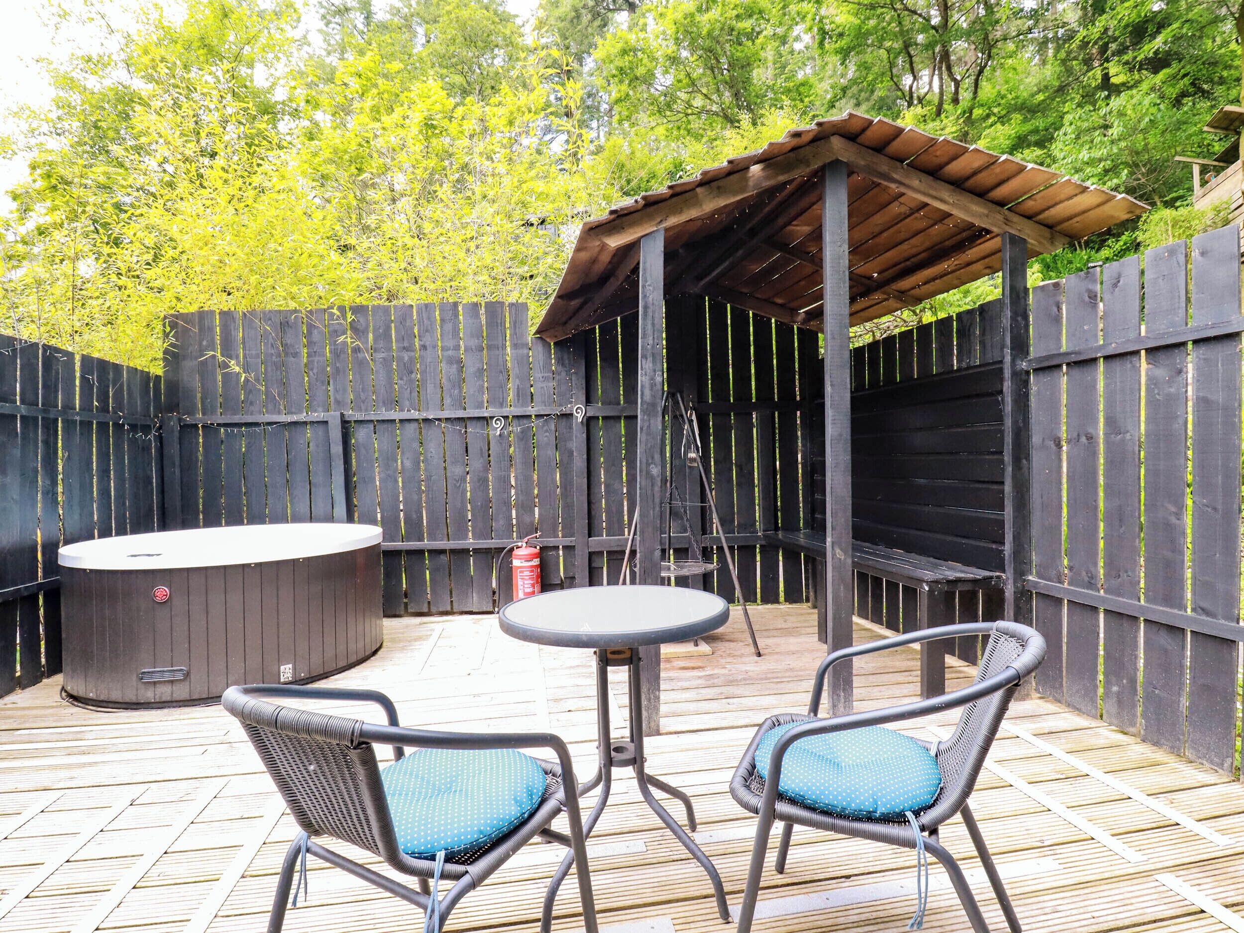 Un patio techado al aire libre con un jacuzzi, dos sillones de mimbre y una mesa.