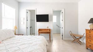 Un dormitorio con cama, mesita de noche de madera, escritorio, silla, cómoda y televisor de pantalla plana montado en la pared.